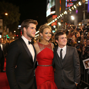 Liam Hemsworth, Jennifer Lawrence, and Josh Hutcherson attending the world premiere of The Hunger Games: Catching Fire. Crowded street with flashing cameras and fans