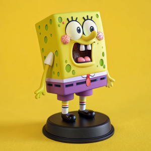 A figurine of SpongeBob SquarePants with big head and surprised face. He is in green and purple shorts with a playful pattern, standing on a black stand. Bright yellow background