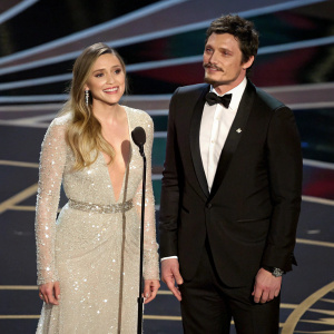 Elizabeth Olsen and Pedro Pascal, elegantly dressed, standing on stage at the Oscars. Podium in front, surrounded by red carpet glamour.