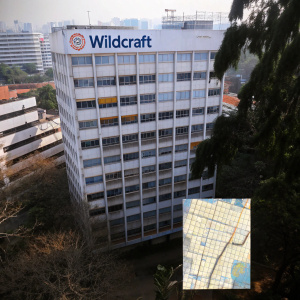 A detailed aerial view of Wildcraft Corporate Office located in bustling Bangalore, India. The office is a modern multi-story building with prominent Wildcraft signage. The map below illustrates the office's position relative to key landmarks and surrounding businesses.