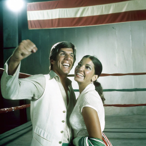 Michael Buffer and Christine Prado at a boxing championship event, smiling for the camera. Colorful boxing ring backdrop.