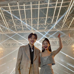 Close-up portrait of Kai from EXO and Jennie from BLACKPINK at a K-pop concert. Strobe lights in background.
