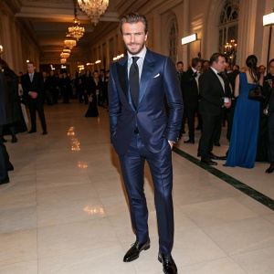 David Beckham, in a sleek navy blue suit, tie, and shiny black dress shoes. Crowded gala event backdrop.
