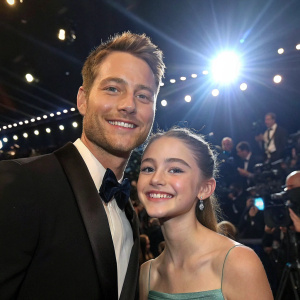 Justin Hartley and Isabella Justice Hartley smiling at an awards ceremony. Bright lights and camera flashes in the background.