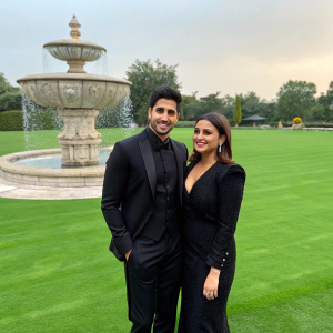 Sidharth Malhotra and Parineeti Chopra, dressed in elegant black suits, stand on a vibrant green lawn. They pose near a grand fountain.