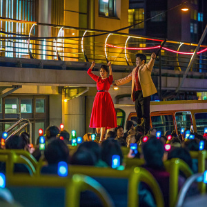 Actors Han Ji-Hye and Yoon Kye-Sang during an energetic dance performance. Han Ji-Hye in a vibrant red dress. Crowded auditorium, flashing lights.