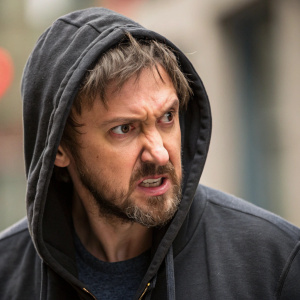 Sam Huntington as Josh Levison from 'Being Human'. Middle-aged man with scruffy beard and intense stare. Wears dark hoodie. Close-up shot, background blurred. Aggressive facial expression.