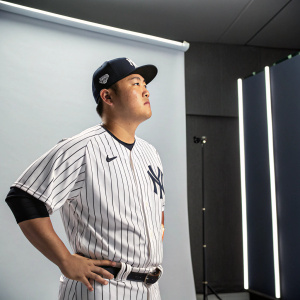 Ji-Man Choi, New York Yankees infielder, standing in a professional studio. Athletic stance, wearing Yankees jersey and cap. Background is sleek, minimalist.