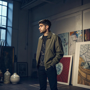 Zayn Malik standing in a dimly lit studio. Surrounded by modern art pieces and abstract installations.