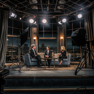 Studio shot of Jay Leno, Martin Short, Kim Caldwell, and Faith Hill on a late night talk show. Bright stage lights and city skyline backdrop