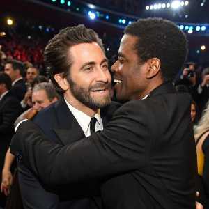 Jake Gyllenhaal and Chris Rock at a crowded award show, embracing. Numerous celebrities and fans in the background.