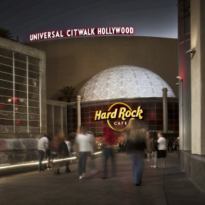 Photograph of Universal CityWalk Hollywood at night. Illuminated Hard Rock Cafe sign, glowing dome, and neon lights. Crowds of people.