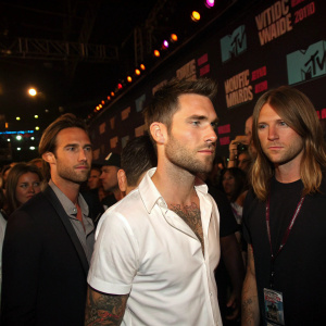 Maroon 5 band members Adam Levine, James Valentine, and Mickey Madden at the MTV Video Music Awards. Adam in a white shirt with visible tattoo. Background features MTV logos. Crowded event, dimly lit.