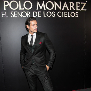 Polo Monarrez in a sharp black suit and tie, stands out at the El Senor De Los Cielos season 5 premiere. Dignified pose against a sleek black backdrop. The event logo is prominently displayed.