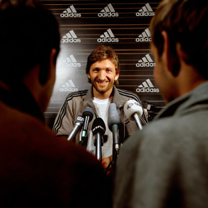 Marko Marin, smiling confidently at a press conference. Adidas logo prominent on backdrop. Microphones surrounding him.