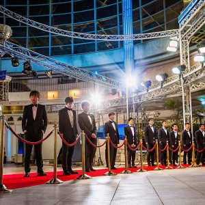 EXO members in black tuxedos, hairstyles sleek and groomed, posing at the Seoul K-pop Awards. Indoor venue, spotlight on stage