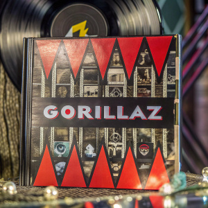Close-up of the Humanz album cover by Gorillaz. A striking red background with geometric shapes and band name prominently featured. Intimate photography style.