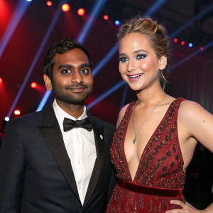 Aziz Ansari and Jennifer Lawrence at the Gotham Awards. Wearing formal attire. Strobe lights in background