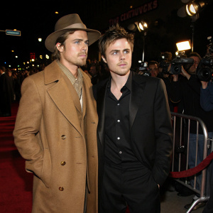 Brad Pitt and Casey Affleck at the Hollywood premiere of 'The Assassination of Jesse James by the Coward Robert Ford'. Pitt in a brown trench coat and wide-brimmed hat, Affleck in sleek black suit. Crowded red carpet with flashing cameras.