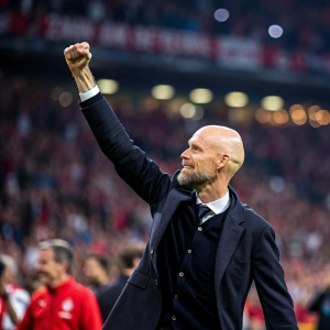 Erik Ten Hag, a bald caucasian man, celebrating with a raised fist. He's wearing a dark suit. Crowded stadium background