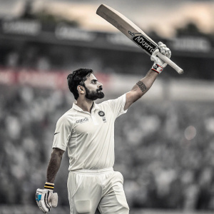 Virat Kohli, Indian cricketer, standing in batting stance. Wearing white uniform. Cricket bat raised, blurred stadium crowd in background.