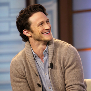 Jonathan Tucker, with a warm smile, in a cozy sweater over a casual shirt. At a Q&A session. Studio backdrop with soft light