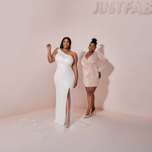 Kimora Lee Simmons and Joanne Perkins attending a glamorous boutique launch. Kimora in a white gown with silver heels, Joanne in a pink dress with matching heels. The backdrop features JustFab branding.