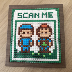Crafted Minecraft-themed QR code, featuring cartoon characters in simple design. Colors: blue, brown, green. Label reads 'SCAN ME'.