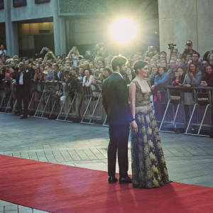 Jake Gyllenhaal and Gemma Arterton attending the premiere of a highly anticipated film. Both are dressed formally. Jake in a sleek black tuxedo, Gemma in a gown with elaborate embroidery. Crowds of photographers and fans in the background.
