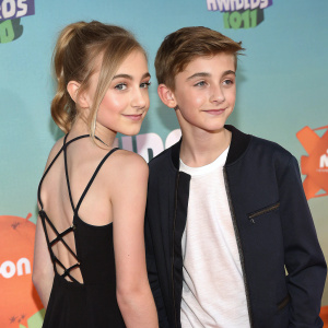 Lauren Orlando and Johnny Orlando, siblings, posing at the 2016 Nickelodeon Kids' Choice Awards. Lauren in black dress with crisscross back detail, Johnny in dark jacket and white t-shirt. Event logo visible in background.