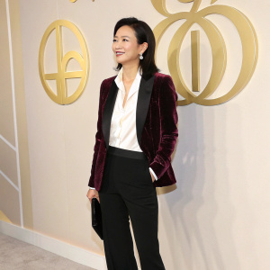 Xu Jinglei, Chinese actress and filmmaker, in a velvet blazer, white blouse, and black pants. Gold logo background at a gala event.