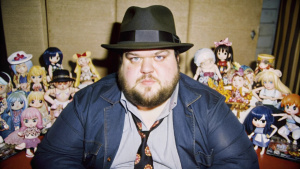 Fat, Greasy Neckbeard Nerd wearing a trilby and surrounded by anime waifu merchandise
