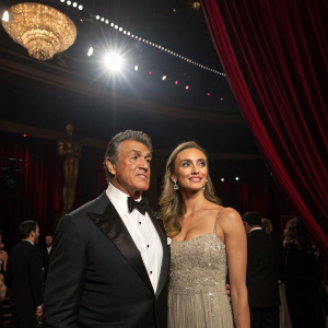 Sylvester Stallone and Katy Russo at a glitzy awards show. Dark, opulent venue, spotlight on them.