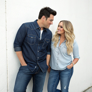 Frankie Moreno and Lacey Schwimmer at a casual gathering. Wearing jeans and casual shirts. A plain white wall serves as backdrop.