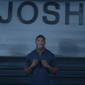 Anthony Joshua, smiling confidently in a blue polo shirt. Standing against a bright yellow backdrop with his name 'Josh' in bold letters.
