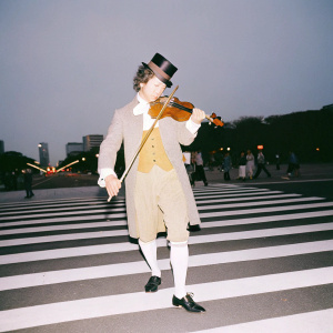 a classical musician from 1800 playing violin on a crowded crosswalk in China. A lot of people are walking in front of him.