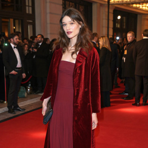Astrid Berges-Frisbey attending an exclusive London charity gala. Dressed in elegant dark red dress and matching velvet coat. Crowded indoor setting with celebrities and dignitaries