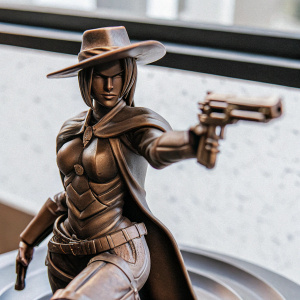 Highly detailed figurine of Ashe from Overwatch. She is sculpted with a dynamic stance, poised to draw her revolver. The figurine sits on a sleek, metallic base that resembles a futuristic stage. She is depicted as a fierce and determined character, wearing a short, angled bob haircut and a wide-brimmed western hat.