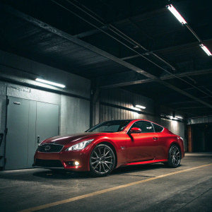 An Infiniti G37 Coupe in vibrant red parked in a dimly lit garage. The car's sleek lines and brand logo stand out against the dark backdrop, creating a stark contrast of light and shadow.
