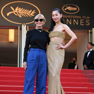Miuccia Prada and Lisa from BLACKPINK on the Cannes Film Festival red carpet. Miuccia in black top and blue pants, Lisa in gold sequined dress.