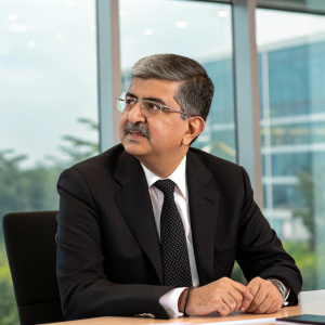 Uday Kotak, the executive vice chairman of Kotak Mahindra Bank, in a professional meeting. He is dressed in a black suit and tie, with a neatly trimmed mustache. The background is a modern office with large windows.
