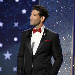 Jon Bernthal at the Critics Choice Awards. Wearing a black tuxedo with a red bow tie, standing against a glittering, starlit sky backdrop.