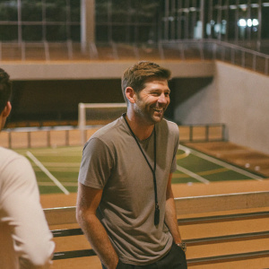 Steven Gerrard, former Liverpool FC captain, in a candid shot. He's smiling, dressed casually. Modern sports facility backdrop.
