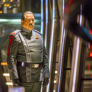 Edward James Olmos as Commander William Adama. Wearing a Star Trek-inspired uniform. Dark, futuristic setting with blurred background.