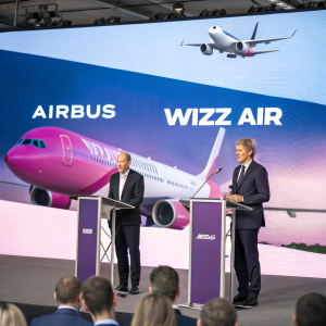 Press event featuring Airbus and Wizz Air leaders. A giant screen showcasing airline advertisement behind them.