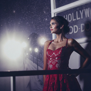 Nina Dobrev at the Oscar Gala, wearing a stunning red dress with intricate lacework and fitted silhouette. The backdrop features the Hollywood sign