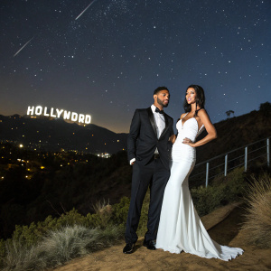Jermaine Pennant in black tuxedo, Alice Goodwin in elegant white gown. Standing in front of Hollywood sign, night sky backdrop