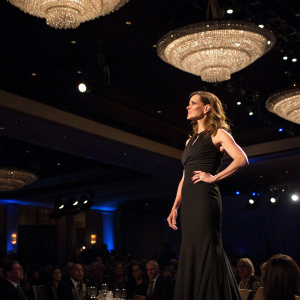 Hilary Swank, sporting a sleek black dress, takes center stage at the awards gala. Surrounded by dimly lit chandeliers and murmuring guests.