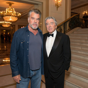 Ray Liotta and Robert Kirbyson at a charity gala. Ray in jeans and casual shirt, Robert in tuxedo. Elegant ballroom setting.