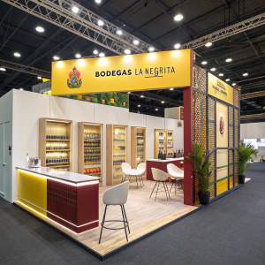 Trade show booth for Bodegas La Negrita. Bright and vibrant color scheme. Central display with tequila branding. Modern furniture and sleek design elements.